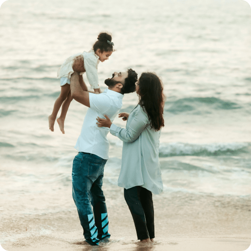 Eltern halten ihr Kind lächelnd hoch in die Luft am Strand.