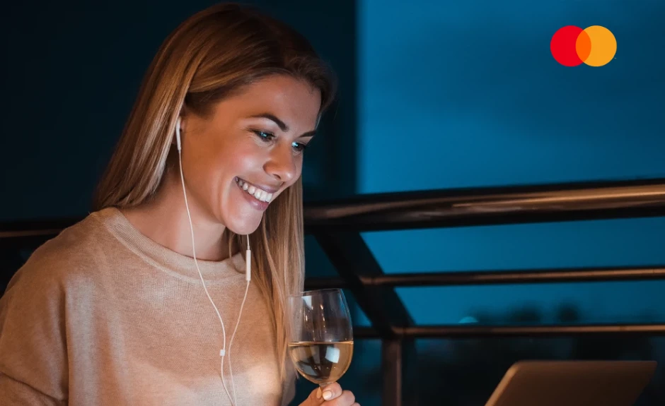 Mastercard Priceless Cashback Blog Header. Eine Frau sitzt im Dunkeln am ihren Laptop und lächelt in den Bildschirm.