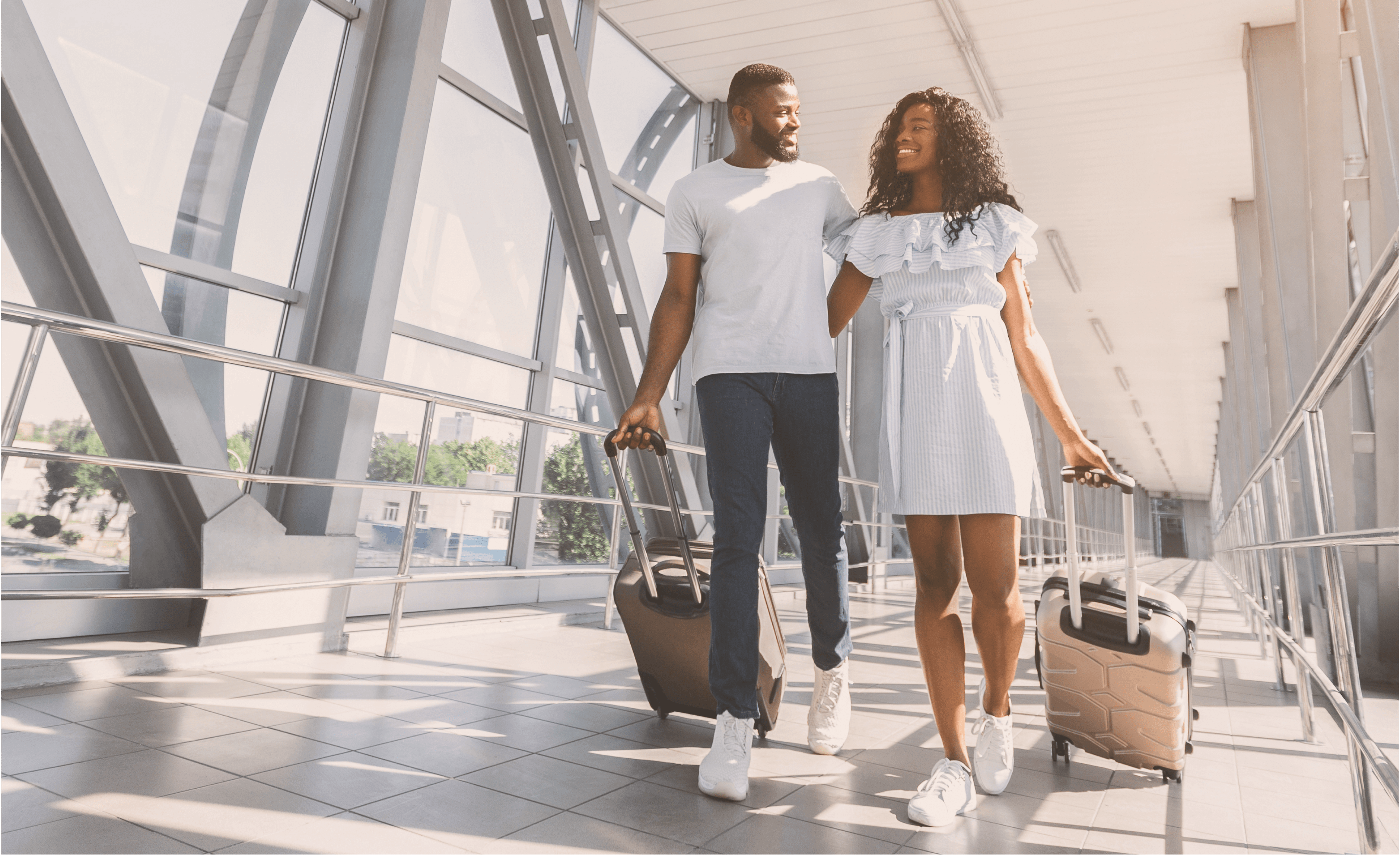 Pärchen läuft lächelnd Arm in Arm am Flughafen und ziehe Koffer hinter sich her.