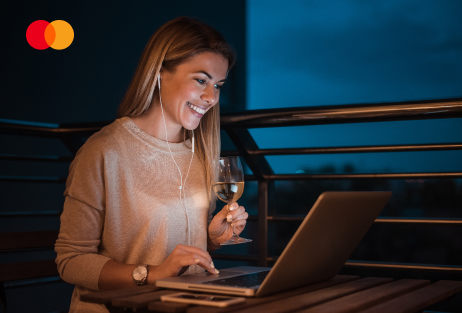 Frau schaut im dunkeln auf den beleuchten Display eines Laptops. Oben links wird das Mastercard Logo angezeigt.