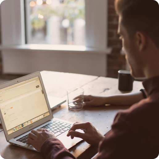 Mann sitzt am offenen Laptop an einem Tisch.