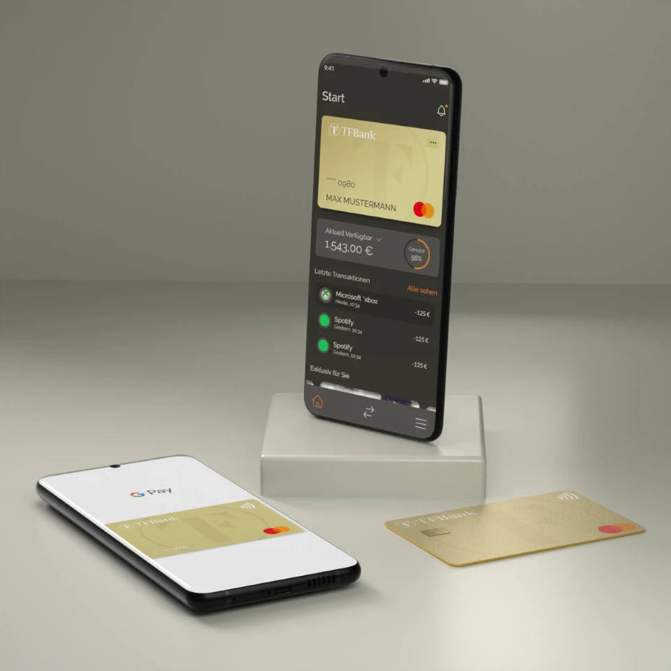 Smartphone steht in einem Raum auf einem  Sockel. Es wird der Home Bildschirm der TF Bank Mobile App angezeigt. Neben dem Sockel liegt ein weiteres Smartphone mit der Google Pay Funktion, sowie eine physische TF Mastercard Gold.