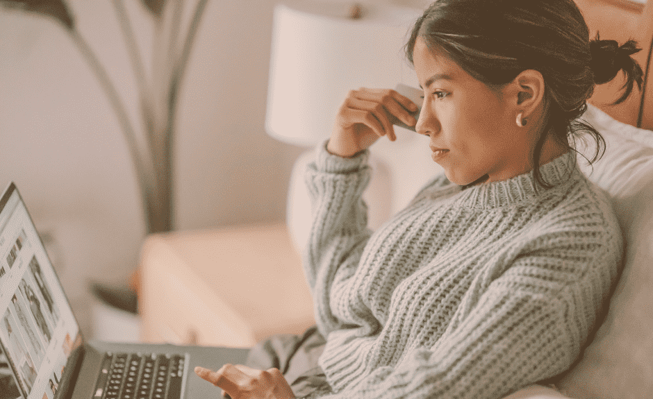Frau sitzt auf Couch und schaut konzentriert auf Laptop beim Online Shopping.