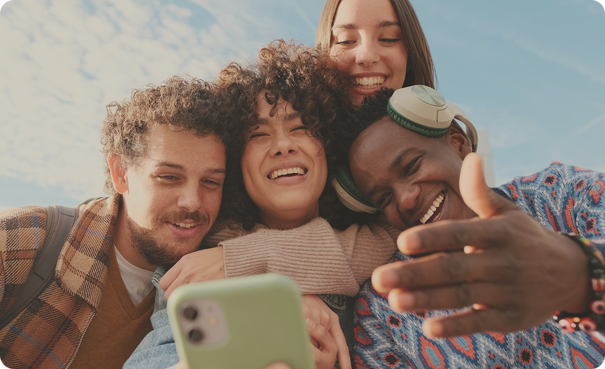 Freunde schauen lachend zusammen in ein Smartphone und umarmen sich.