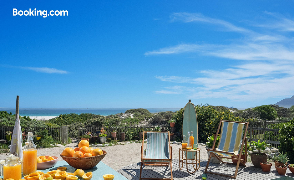 Blauer Himmel und Sicht auf den Strand. Im Vordergrund aber Pool mit 2 Liegestühlen und Orangen 
