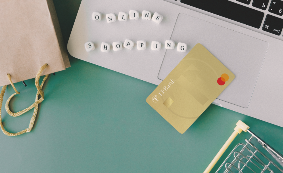 TF Mastercard Gold liegt auf Laptop. Daneben liegen kleine Würfel mit Buchstaben zusammengesetzt als "Online Shopping". Außerdem liegt dort eine kleine Tüte und eiin kleiner modelhafter Einkaufkorb.