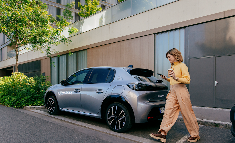 Frau läuft mit Handy in der Hand Richtung Auto, um Carsharing-Angebot mit der TF Mastercard Gold zu buchen