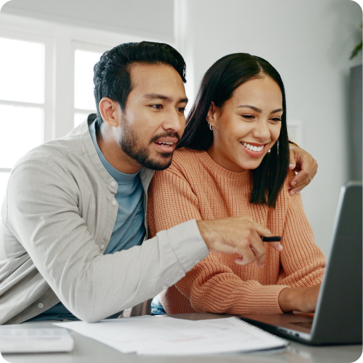 Ein Mann und eine Frau schauen beide auf einen Laptop. Der Mann hat seinen Arm um die Frau gelegt und schaut interessiert. Die Frau lächelt.