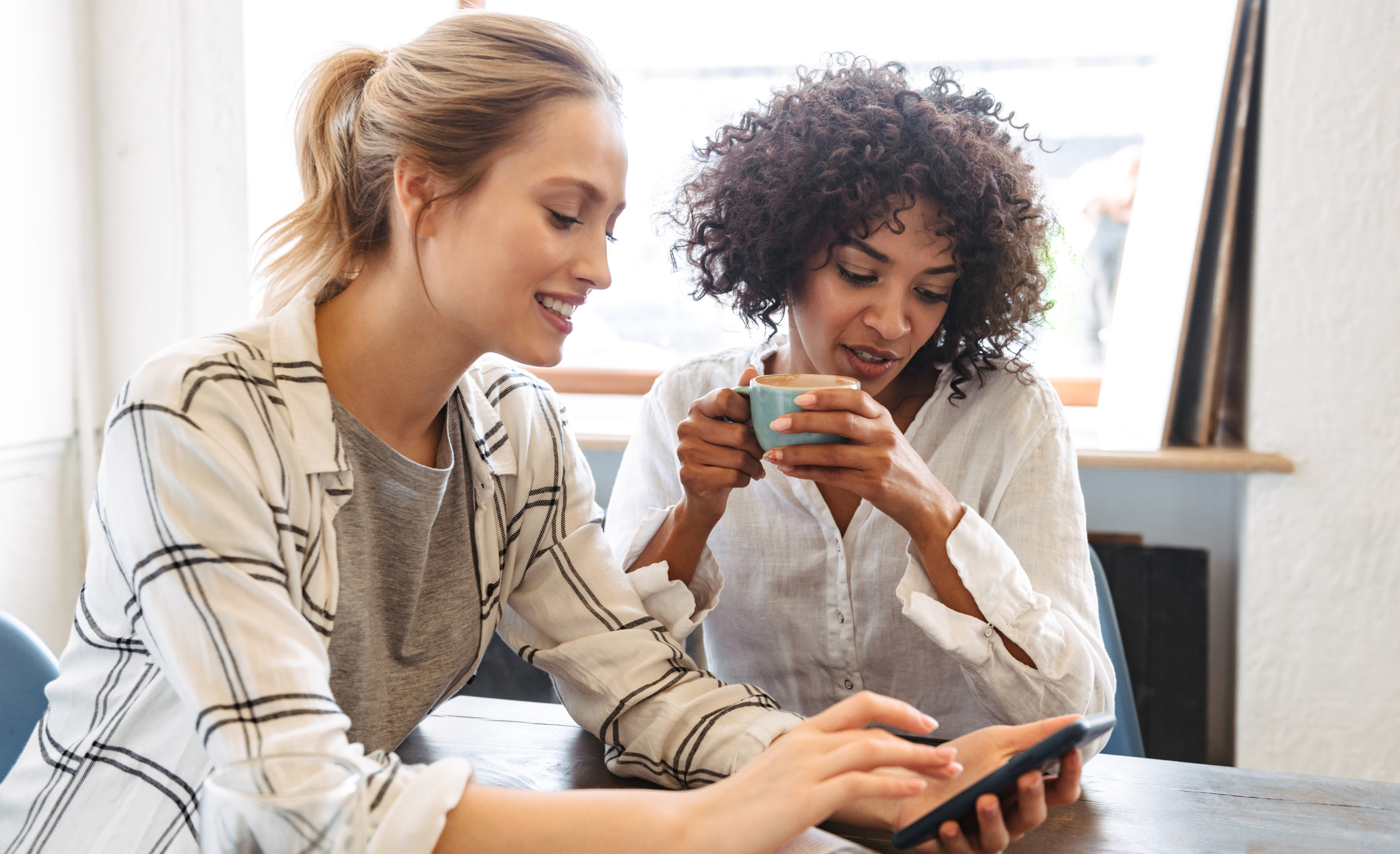 2 Frauen schauen beim Kaffee trinken auf Smartphone, um möglicherweise internationale digitale Zahlung durchzuführen.