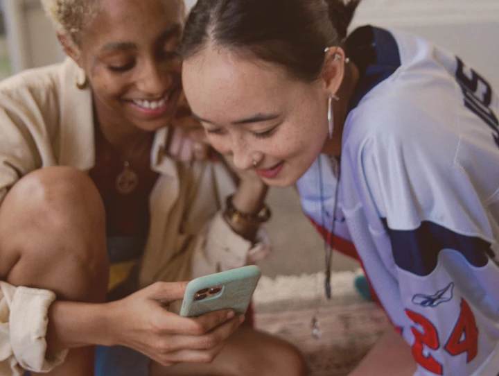 Zwei Freundinnen schauen lächelnd aufs Handy