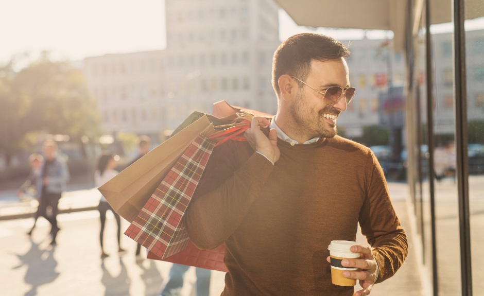 Mann läuft durch die Stadt mit Shoppingtüten und lacht.